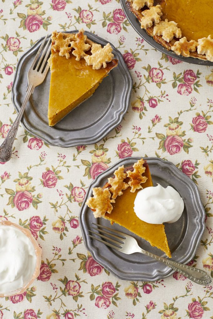 Two slices of Best Ever Pumpkin pie are served on dessert plate with softly whipped cream. They have golden flaky crust, orange golden filling.