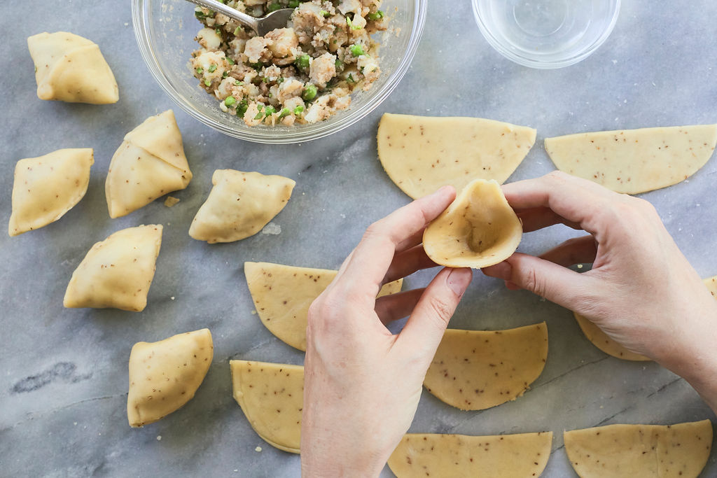 Hands holding a folded Samosa, ready for filling.