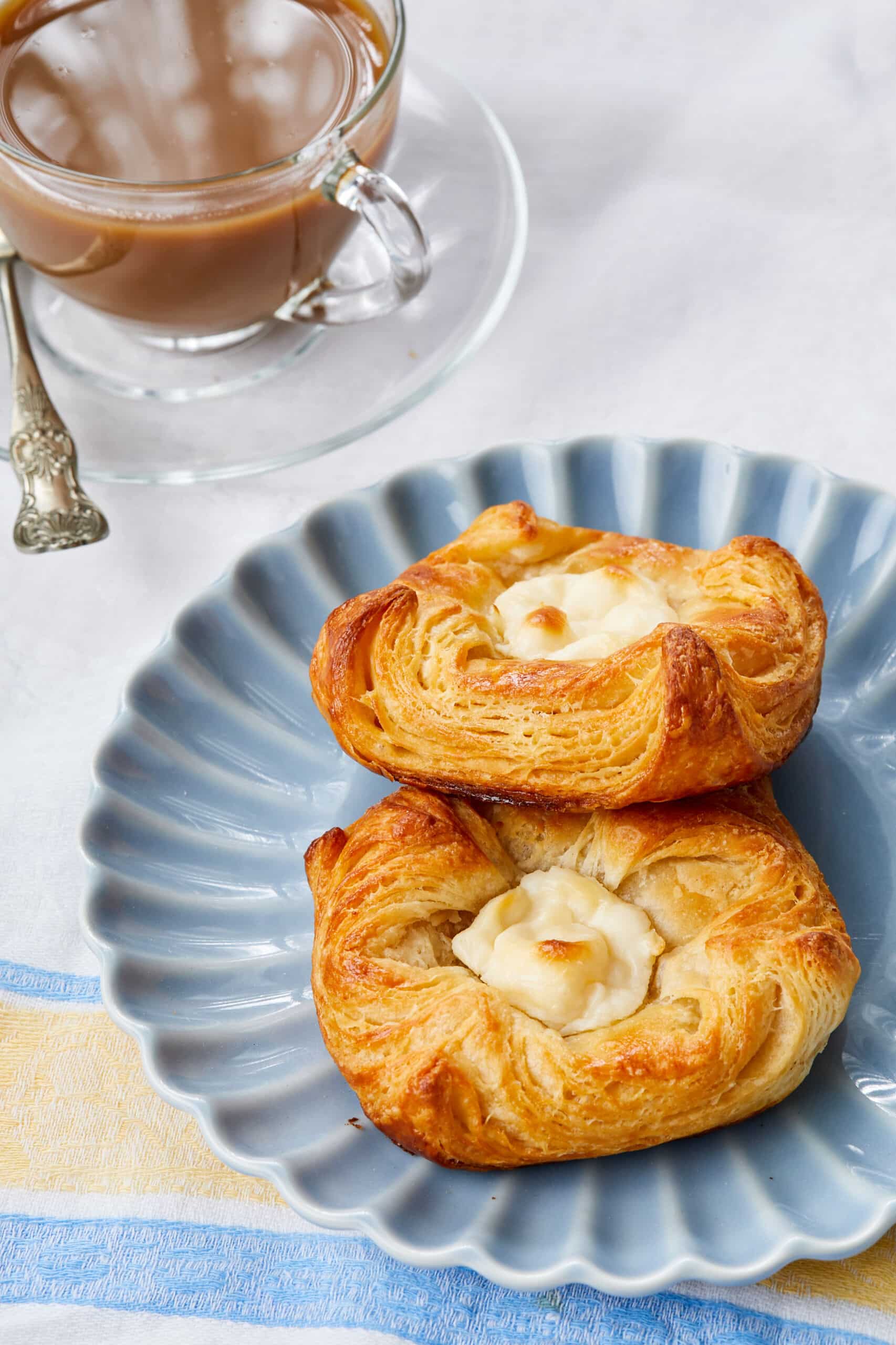 Two golden, flaky Cheese Danish are served with a cup of tea.