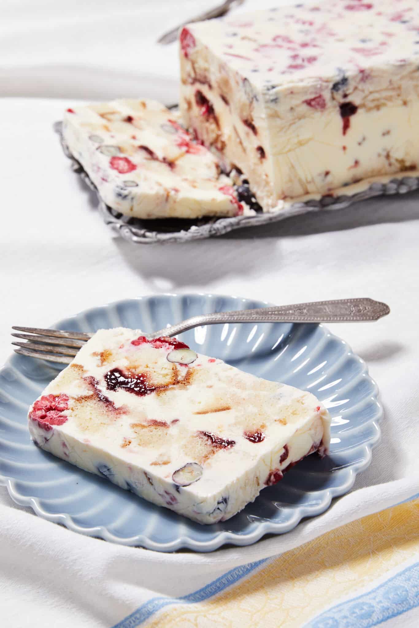 A loaf of Frozen Sherry Berry Trifle is packed with ice cream, berries, raspberry jam, and sherry-soaked, cubed pound cake. One slice is served on a dessert plate.