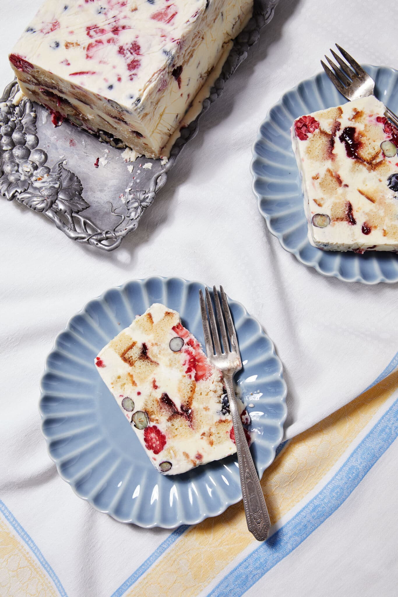 A top-view shot shows a loaf of Frozen Sherry Berry packed with ice cream, berries, raspberry jam, and sherry-soaked, cubed pound cake. Two slices are served on dessert plates.