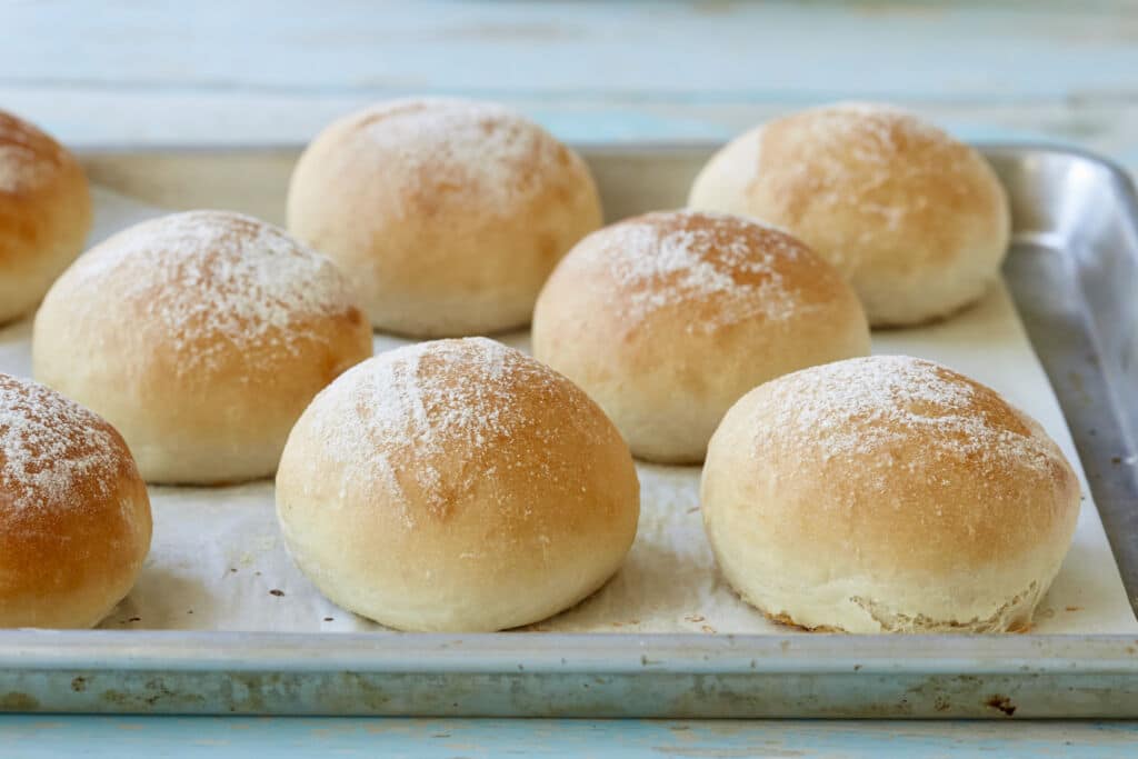 A tray of soft, fluffy Scottish Baps are lightly dusted with flour.