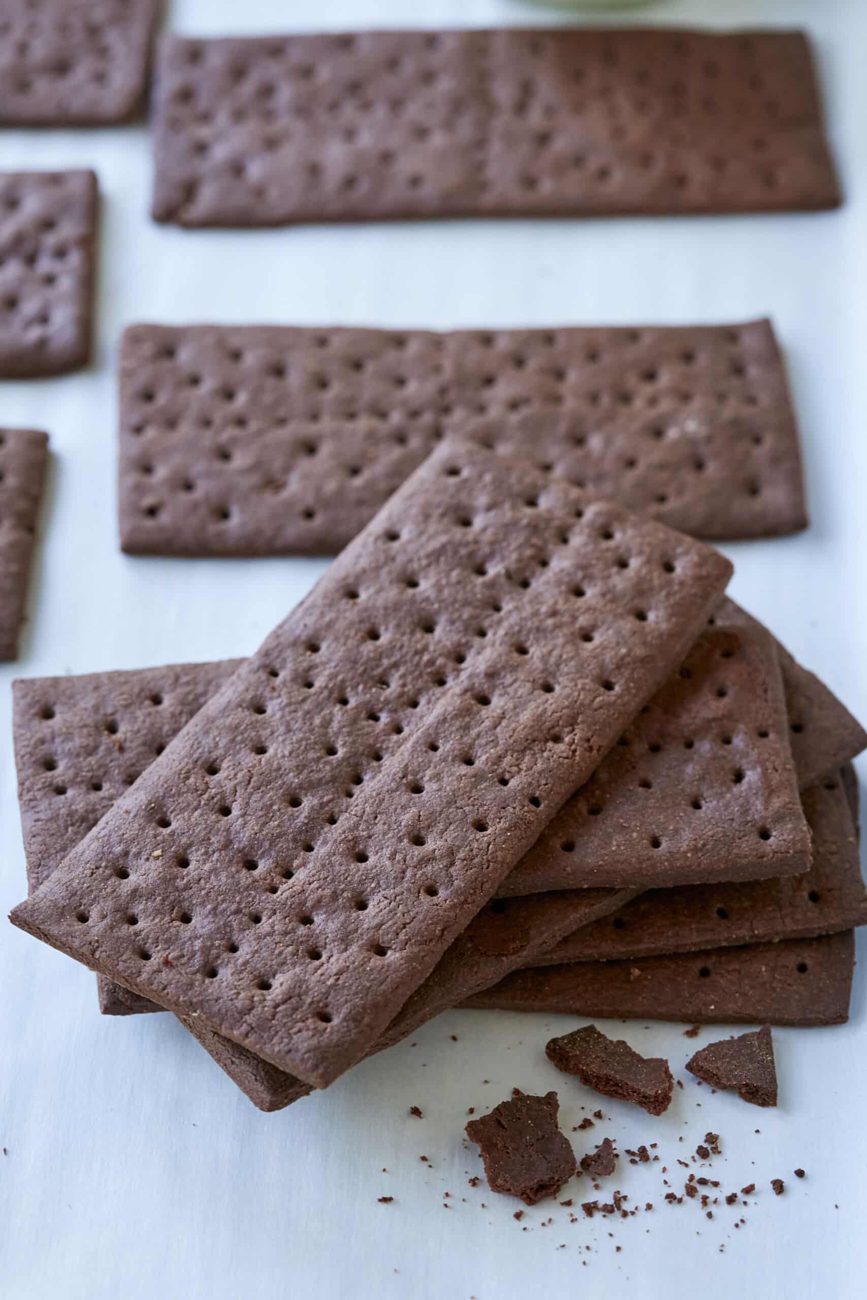 A close-up shot at a stack of Homemade Chocolate Graham Crackers shows the dark chocolate color and crumbly crispy texture.