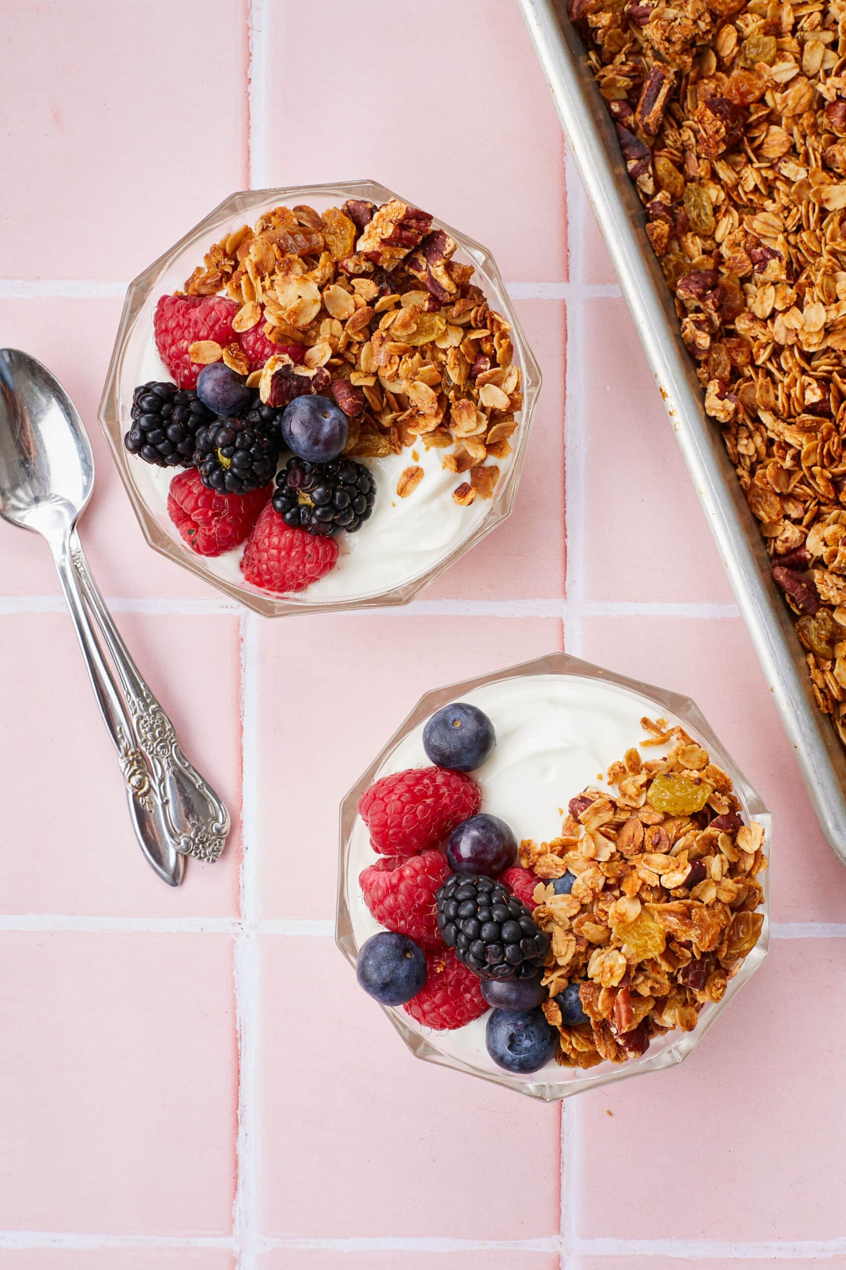 A tray of Healthy Granola (No refined sugar, baked golden brown all over, packed with oats, nuts, and raisins. They're served with yogurt, fish blueberries, raspberries, and blackberries.