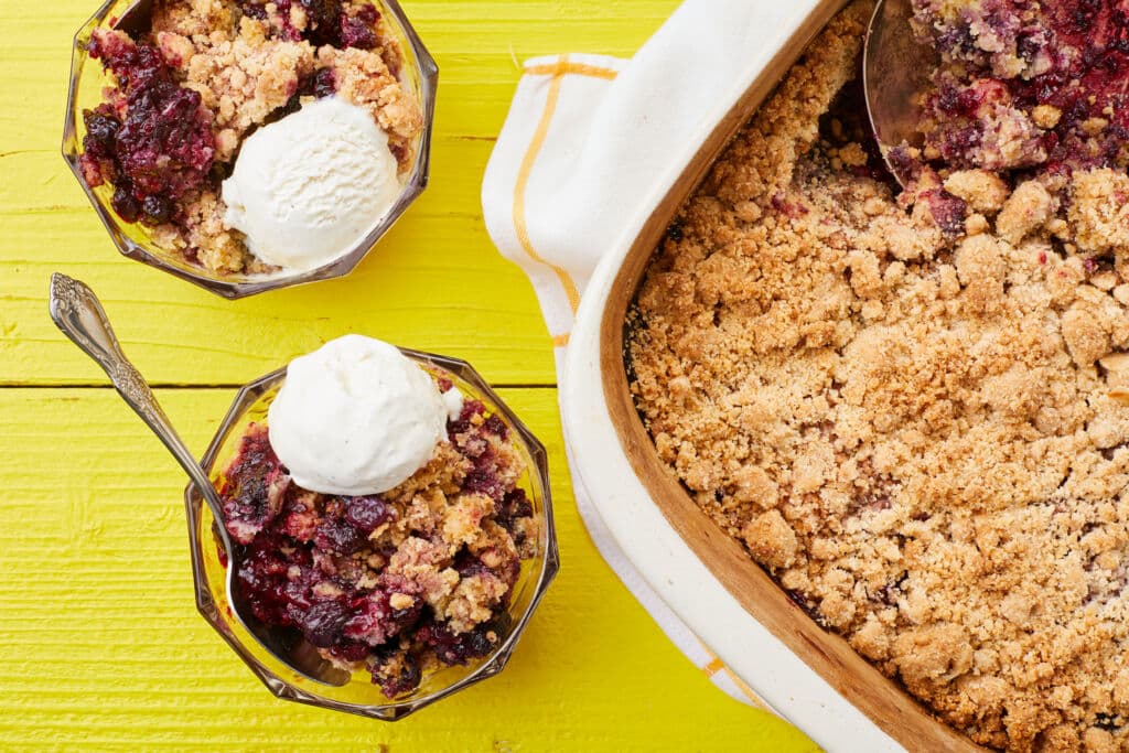 Mixed Berry Cobbler with Cake Mix is served in dessert bowls with ice cream on top. The rest of the cobbler is in the baking dish with golden crumbly soft topping and bubbly fruit filling.