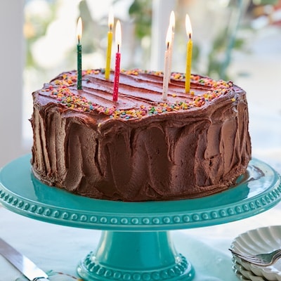 A Best-Ever Yellow Cake with luscious whipped ganache frosting is on a turquoise color cake stand. It's perfect treat for a birthday with candles on it.